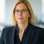 Sophia Schmidt Porträtfoto von Sophia Schmidt, der Steuerspezialistin des Unternehmens. Sie ist eine Frau mit schulterlangem blondem Haar und trägt eine Brille. Sie hat einen professionellen und fokussierten Ausdruck. Sie trägt einen dunkelblauen Blazer über einer passenden Bluse. Der Hintergrund ist modern und leicht unscharf, was eine Büroumgebung andeutet.